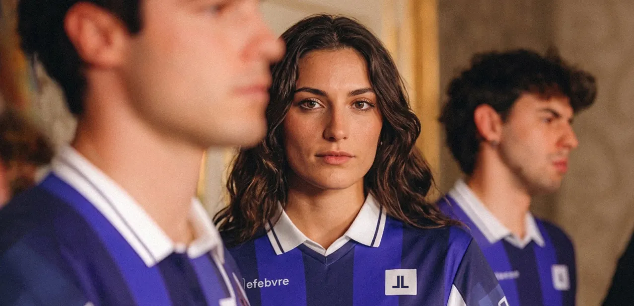 Tres jóvenes con la camiseta azul de Lefebvre en una sala; en el centro, una joven mira a cámara